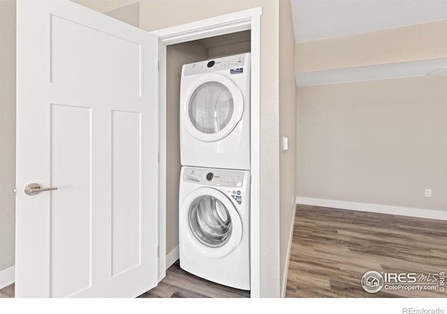 clothes washing area with stacked washer and dryer, dark wood-style flooring, laundry area, and baseboards