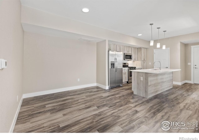 kitchen featuring a kitchen island with sink, a sink, light countertops, appliances with stainless steel finishes, and hanging light fixtures