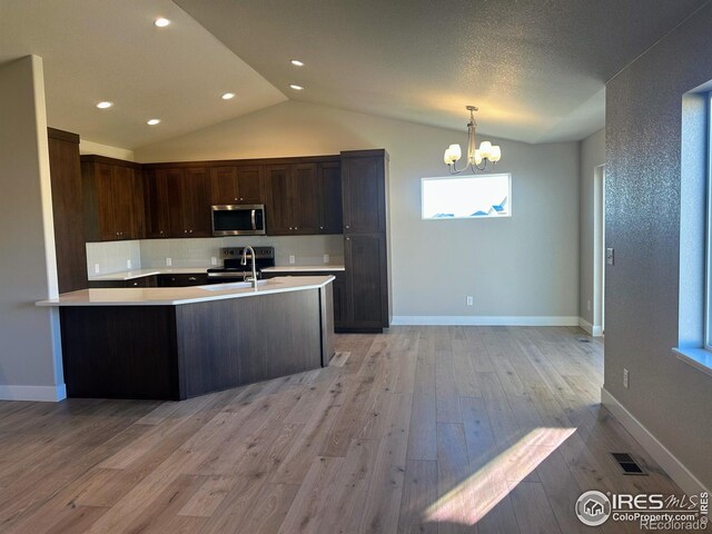 kitchen featuring lofted ceiling, hanging light fixtures, light wood-type flooring, appliances with stainless steel finishes, and a chandelier