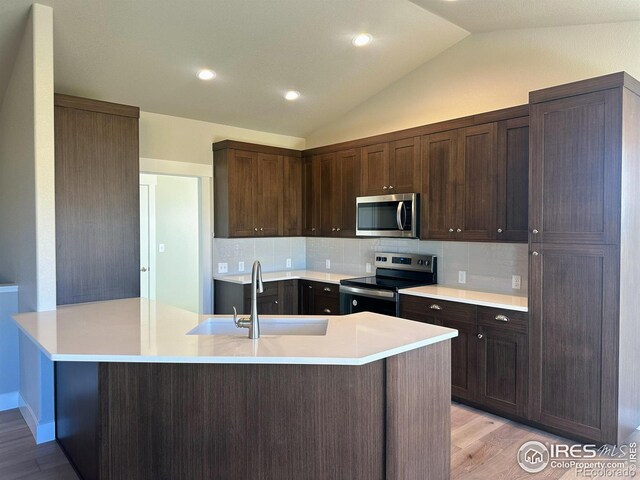 kitchen with sink, stainless steel appliances, tasteful backsplash, lofted ceiling, and light wood-type flooring