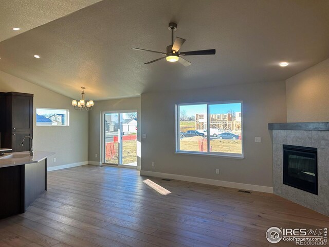 unfurnished living room with a tile fireplace, sink, light hardwood / wood-style floors, a textured ceiling, and lofted ceiling