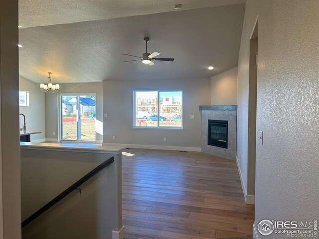 unfurnished living room featuring ceiling fan with notable chandelier, hardwood / wood-style flooring, a wealth of natural light, and a tiled fireplace