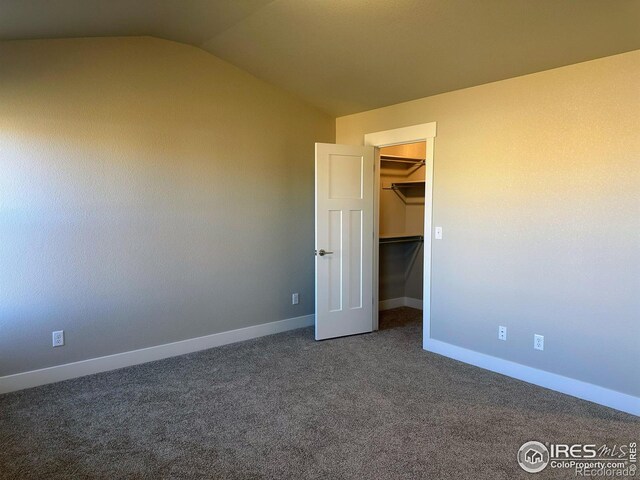 unfurnished bedroom with a walk in closet, a closet, dark carpet, and vaulted ceiling