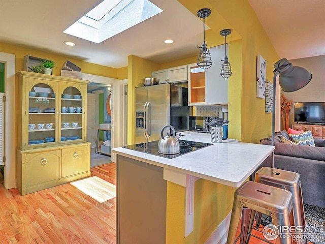 kitchen featuring kitchen peninsula, a kitchen breakfast bar, a skylight, decorative light fixtures, and stainless steel fridge with ice dispenser