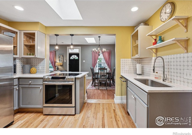 kitchen featuring appliances with stainless steel finishes, a skylight, sink, decorative light fixtures, and light hardwood / wood-style flooring