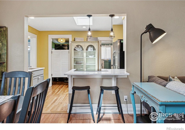 kitchen featuring a skylight, a kitchen breakfast bar, stainless steel fridge with ice dispenser, pendant lighting, and light hardwood / wood-style floors