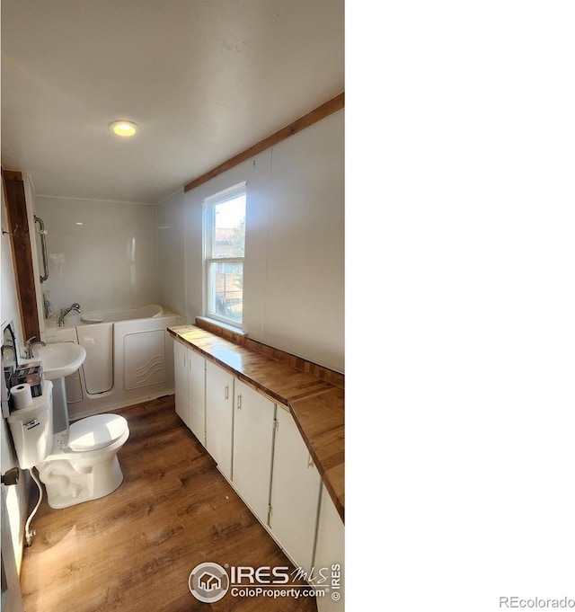 bathroom with wood-type flooring, a tub to relax in, and toilet