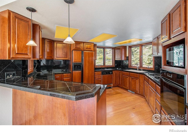 kitchen featuring backsplash, black appliances, sink, light wood-type flooring, and kitchen peninsula