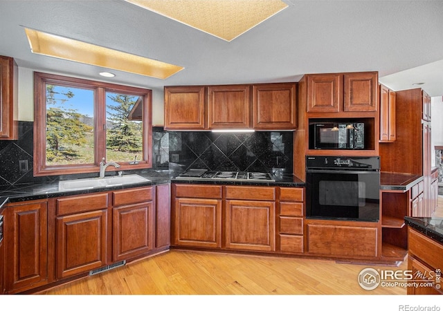 kitchen featuring backsplash, sink, black appliances, and light wood-type flooring