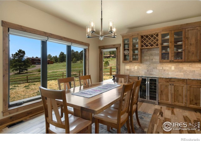 dining room with a chandelier, bar, wine cooler, and light wood-type flooring