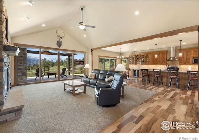 living room with high vaulted ceiling, ceiling fan with notable chandelier, a fireplace, and light hardwood / wood-style floors