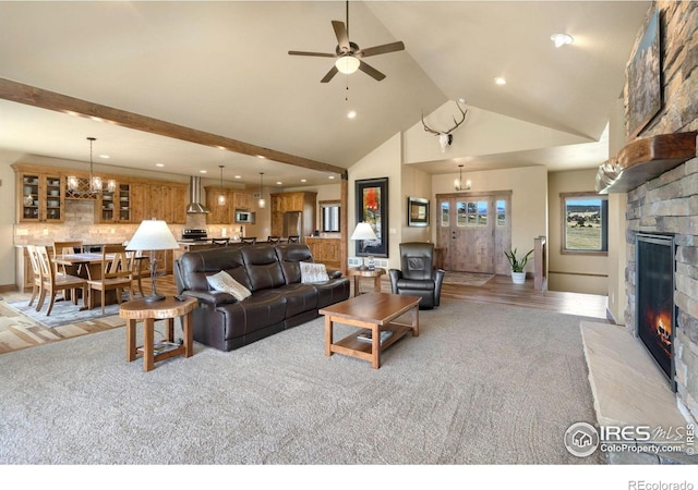 carpeted living room with a stone fireplace, ceiling fan with notable chandelier, and high vaulted ceiling