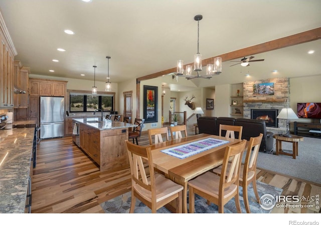 dining area with dark wood-type flooring, a stone fireplace, ceiling fan with notable chandelier, and sink