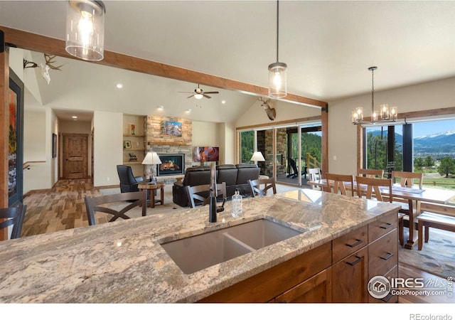 kitchen with hanging light fixtures, a fireplace, light stone countertops, lofted ceiling with beams, and ceiling fan with notable chandelier