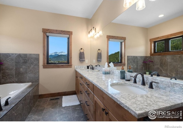 bathroom featuring a relaxing tiled tub, plenty of natural light, and vanity