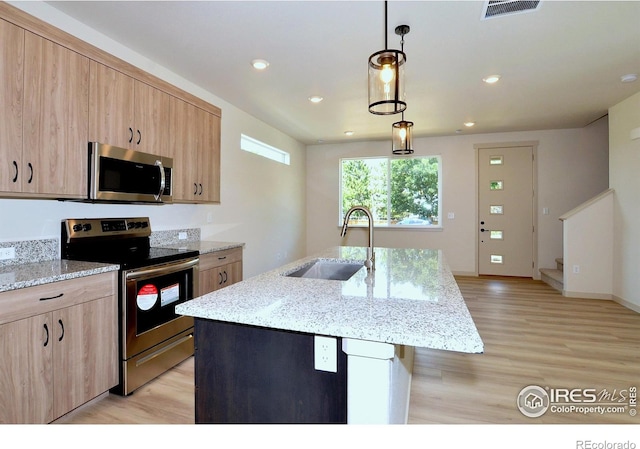 kitchen featuring sink, pendant lighting, appliances with stainless steel finishes, and an island with sink