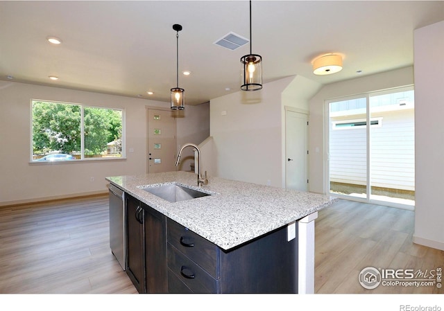 kitchen featuring light stone countertops, pendant lighting, dishwasher, an island with sink, and sink