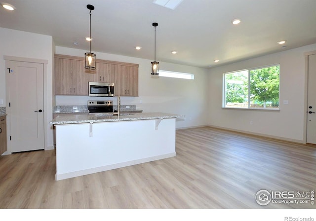 kitchen featuring light stone countertops, stove, a kitchen breakfast bar, light wood-type flooring, and decorative light fixtures