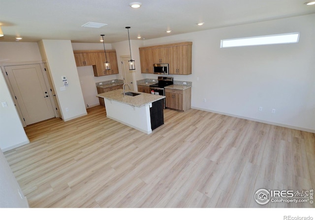 kitchen with a kitchen island with sink, light wood-type flooring, decorative light fixtures, sink, and stainless steel appliances