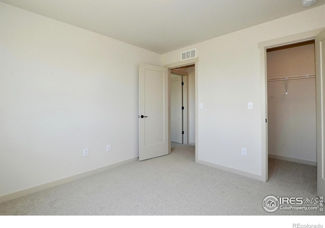 unfurnished bedroom with a walk in closet, light carpet, and a closet