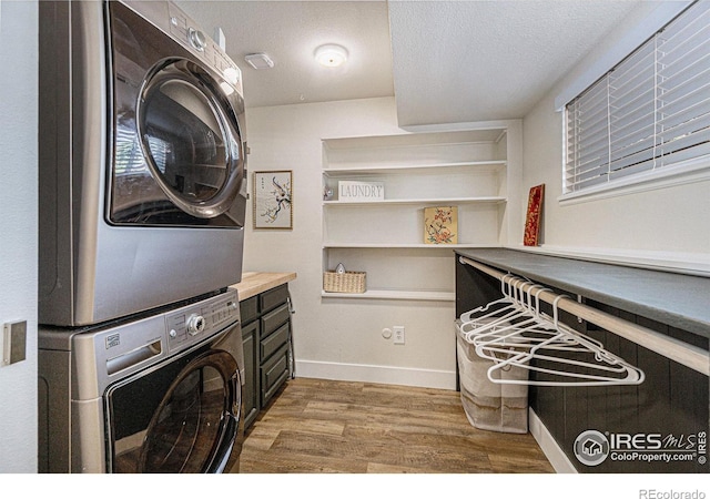 washroom with laundry area, stacked washer and dryer, light wood finished floors, baseboards, and a textured ceiling