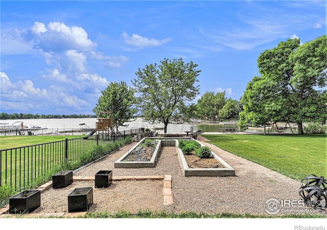 view of property's community featuring a water view, fence, a vegetable garden, and a lawn