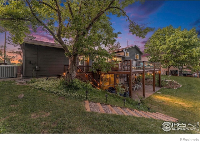 back of property at dusk with a patio, cooling unit, a lawn, and a wooden deck