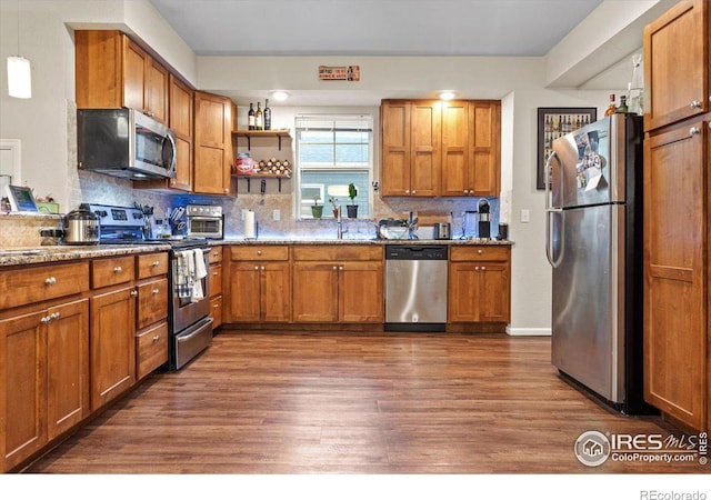 kitchen featuring sink, dark wood-type flooring, stainless steel appliances, light stone counters, and pendant lighting