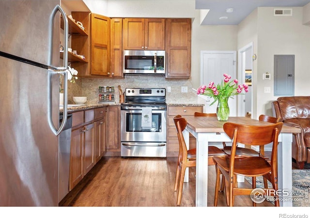 kitchen with appliances with stainless steel finishes, tasteful backsplash, light stone counters, hardwood / wood-style flooring, and electric panel