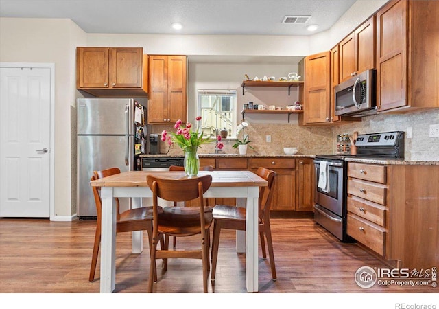 kitchen with wood-type flooring, light stone countertops, stainless steel appliances, and tasteful backsplash