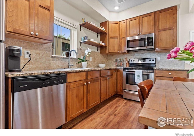 kitchen featuring light stone countertops, sink, stainless steel appliances, tasteful backsplash, and light hardwood / wood-style flooring