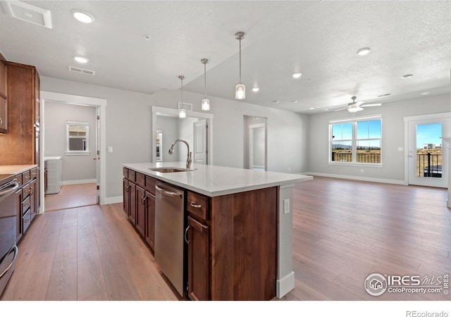 kitchen with light wood-type flooring, ceiling fan, sink, hanging light fixtures, and an island with sink