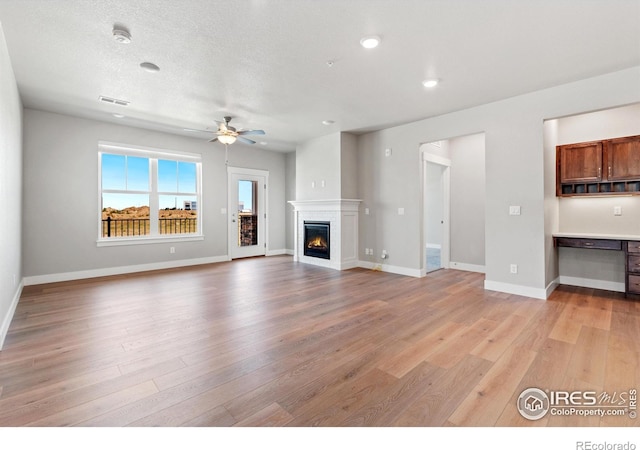 unfurnished living room with ceiling fan, built in desk, light hardwood / wood-style floors, and a textured ceiling