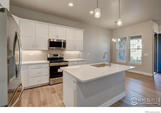 kitchen with white cabinetry, light wood-type flooring, stainless steel appliances, an island with sink, and pendant lighting