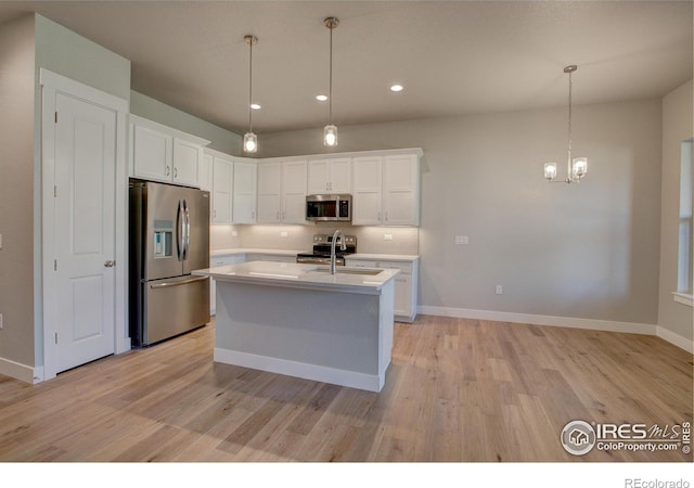 kitchen featuring appliances with stainless steel finishes, light wood-type flooring, an island with sink, and pendant lighting