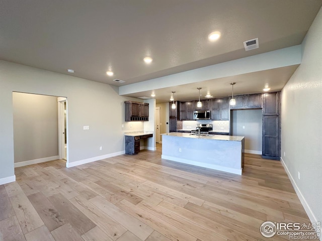 kitchen with dark brown cabinets, appliances with stainless steel finishes, a center island with sink, and light wood-type flooring