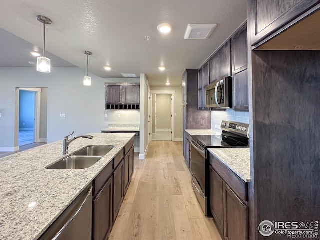 kitchen with decorative light fixtures, sink, light stone counters, light hardwood / wood-style floors, and stainless steel appliances