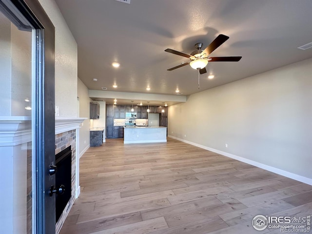 unfurnished living room featuring a fireplace, ceiling fan, and light hardwood / wood-style flooring