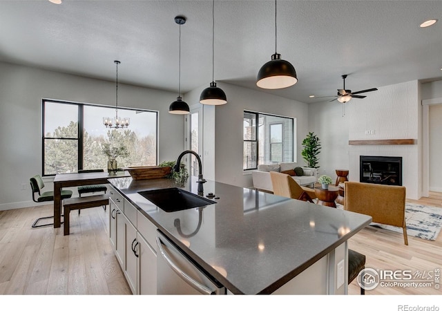 kitchen with sink, white cabinetry, hanging light fixtures, dishwasher, and an island with sink