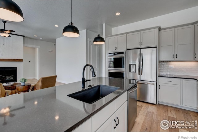 kitchen featuring sink, dark stone countertops, a large fireplace, appliances with stainless steel finishes, and pendant lighting