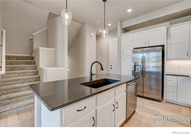 kitchen with white cabinets, appliances with stainless steel finishes, a center island with sink, and sink