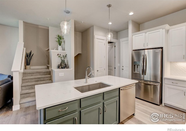 kitchen featuring pendant lighting, a center island with sink, sink, light wood-type flooring, and appliances with stainless steel finishes