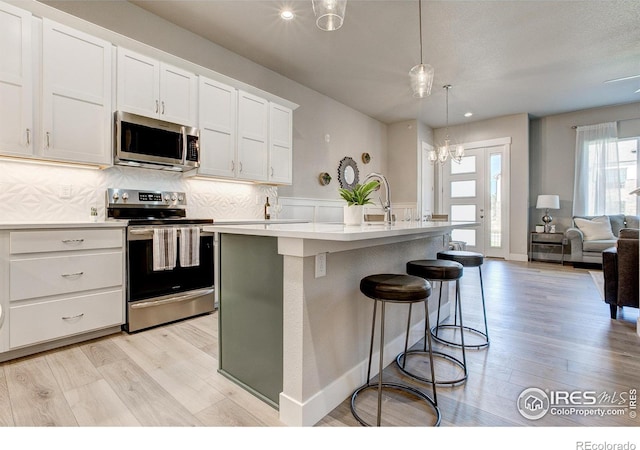 kitchen featuring hanging light fixtures, appliances with stainless steel finishes, light hardwood / wood-style flooring, and a kitchen island with sink