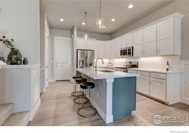 kitchen featuring a kitchen island with sink, sink, appliances with stainless steel finishes, light hardwood / wood-style floors, and white cabinetry