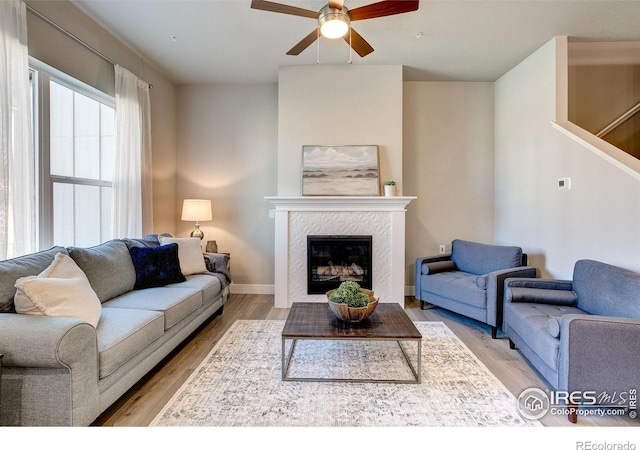 living room featuring a tile fireplace, light wood-type flooring, and ceiling fan