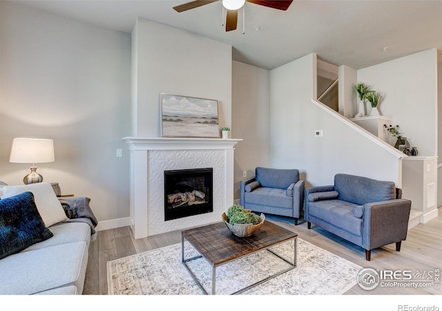 living room with a fireplace, light wood-type flooring, and ceiling fan