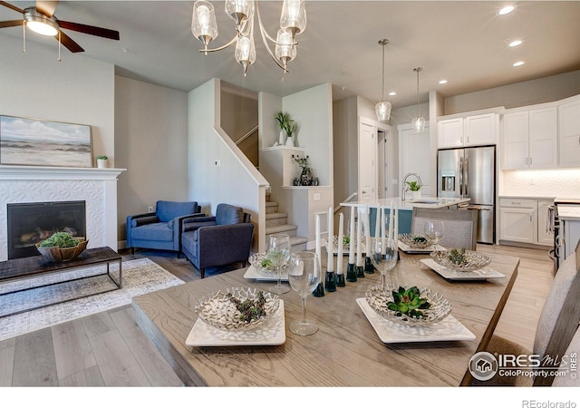 living room with a tile fireplace, light wood-type flooring, ceiling fan with notable chandelier, and sink