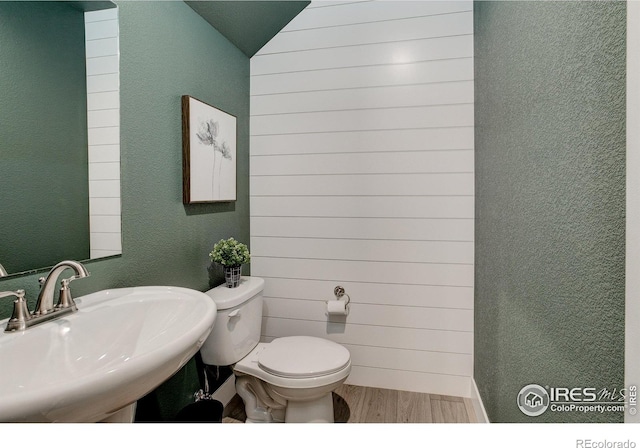 bathroom with sink, wood-type flooring, lofted ceiling, toilet, and wooden walls