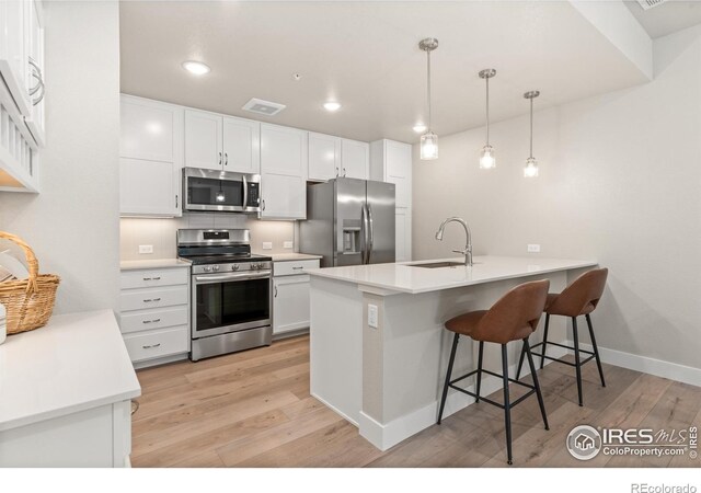 kitchen featuring light wood-type flooring, white cabinets, appliances with stainless steel finishes, sink, and decorative light fixtures