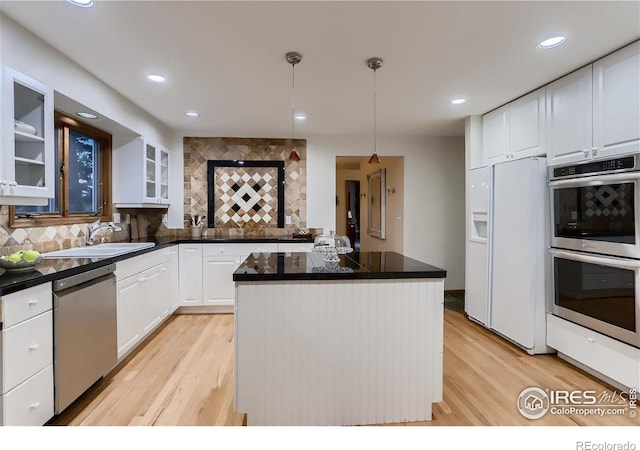 kitchen featuring white cabinets, decorative light fixtures, light wood-type flooring, and stainless steel appliances